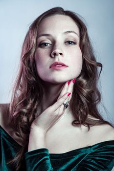 Beauty portrait of confident beautiful woman with brown hair wearing green dress, having red manicure, looking at camera, expressing confidence. Indoor studio shot isolated on gray background.
