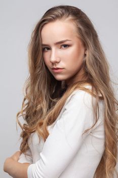 Closeup portrait of beautiful attractive young adult woman with long curly blond hair looking at camera with pensive facial expression. Indoor studio shot isolated on gray background.