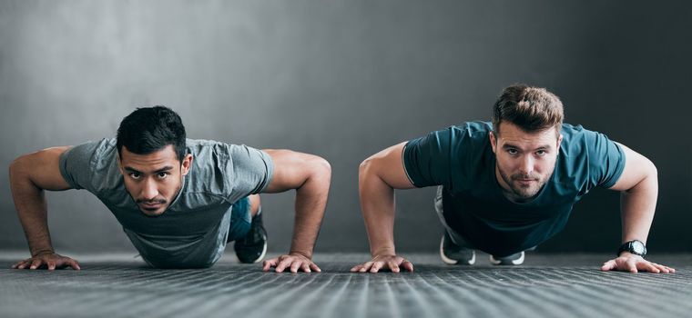 Working on their upper body. Full length portrait of two handsome young male athletes doing pushups side by side against a grey background