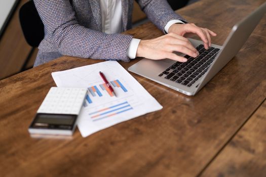 an insurance specialist fills out work papers on a laptop next to it lies a calculator and a graph.