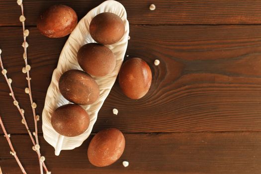 painted eggs on a plate with a sprig of willow on a wooden table. Easter celebration. copy space