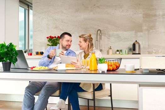 Happy couple working from home and having breakfast together. Breakfast together before leaving for work. Couple having breakfast while using laptop