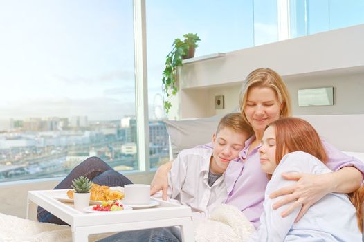 Mother having breakfast in bed with her childrens at mothers day. family breakfast in bedroom. Happy mother with her little daughter and son having breakfast together in bed at home.