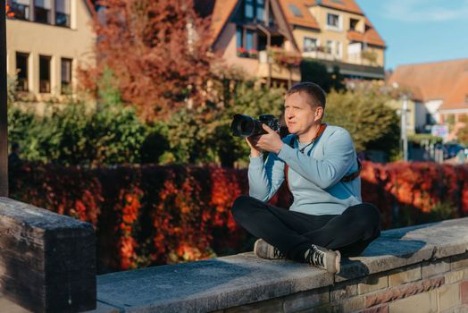 Man Sitting on Stairs in Old European City And Holding Photo Camera. Contemporary Stylish Blogger And Photographer