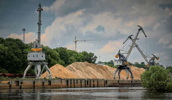 River port in winter. Port cranes on the bank of the river. Embankment of the river port, a barge at the quay wall. Large port cranes on the river. Extraction and transportation of sand other cargo