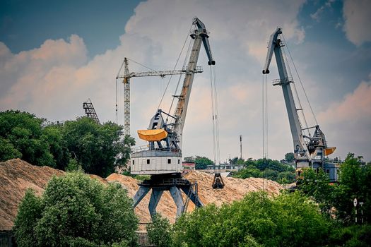 River port in winter. Port cranes on the bank of the river. Embankment of the river port, a barge at the quay wall. Large port cranes on the river. Extraction and transportation of sand other cargo