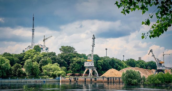 River port in winter. Port cranes on the bank of the river. Embankment of the river port, a barge at the quay wall. Large port cranes on the river. Extraction and transportation of sand other cargo