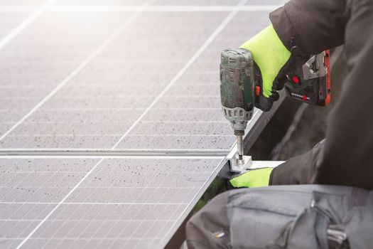 The solar panel installer twists the modules together using aluminum fasteners and a cordless drill. Rooftop installation work and security, concept with copy space.