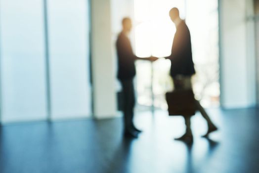 Its the start of doing great things together. Defocused shot of two businessmen shaking hands in an office