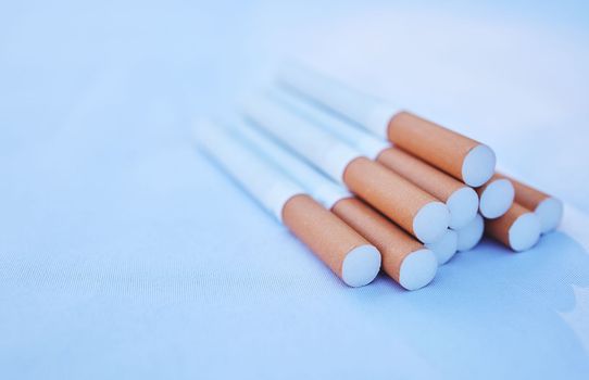 Cigarette, cancer and smoke with a tobacco product on the ground against a blue background to promote awareness. Smoking, toxic and addiction with cigarettes in a pile or stack on the floor.