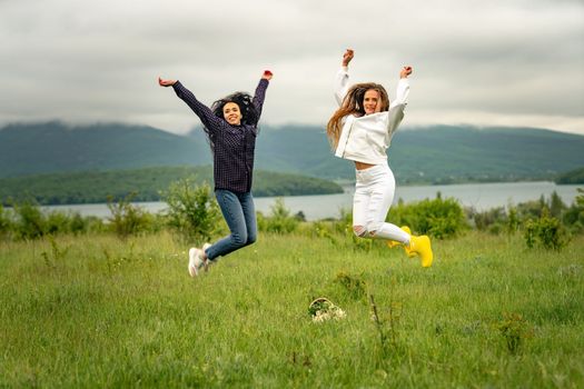 Two girls with long hair are jumping in a clearing overlooking the mountains. The concept of travel and tourism to different countries