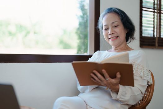 Portrait of an elderly Asian woman in a modern pose holding a memory notebook and operating a computer