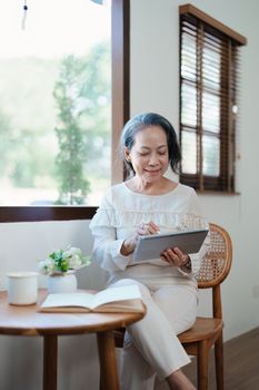 Portrait of an elderly Asian woman in a modern pose working on a tablet computer