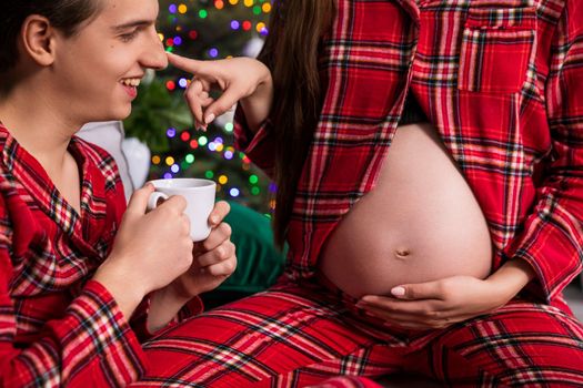 The tip of a man's nose, seen in profile, is touched by a woman sitting next to him. The woman is pregnant, a close-up of a large pregnant belly.