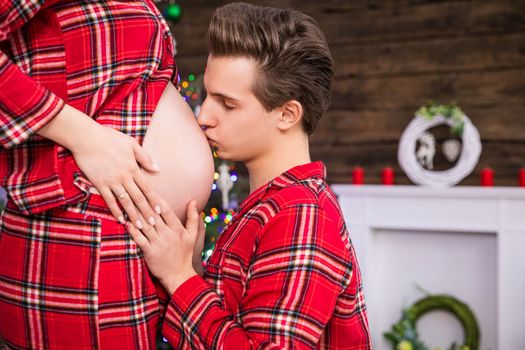 A man kisses hisClose-up in profile on a woman's pregnant belly. The man kneels in front of his partner and kisses the pregnant belly. The couple holds their hands on the side of the pregnant belly. partner's pregnant belly while kneeling in front of her.