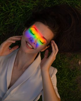 Top view of caucasian woman with rainbow ray on her face lies on green grass