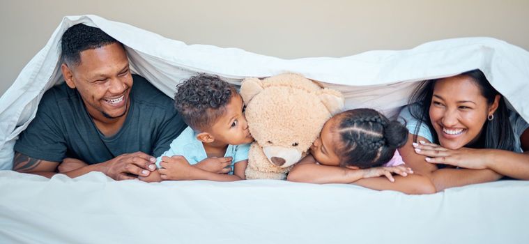 Black family, bed and teddy bear with parents and kids kissing a stuffed animal while lying together in a bedroom. Portrait, love and children inside to relax in the morning with mother and father.