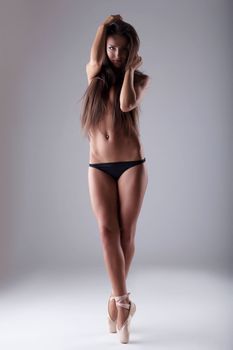 Elegant topless ballet dancer posing in studio, on gray background