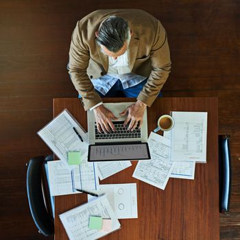 Keeping business moving along. High angle shot of a mature businessman working on a laptop in an office