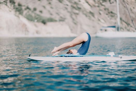 Woman sup yoga. Middle age sporty woman practising yoga pilates on paddle sup surfboard. Female stretching doing workout on sea water. Modern individual hipster outdoor summer sport activity