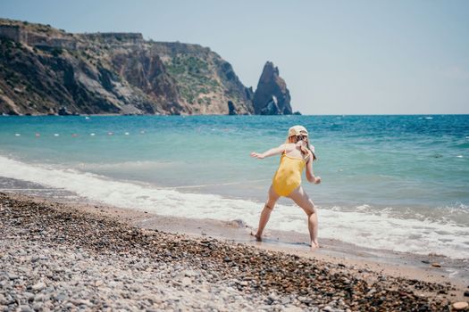 Cute little girl running along the seashore against a clear blue sea and rejoices in the rays of the summer sun. Beautiful girl in yellow swimsuit running and having fun on tropical beach