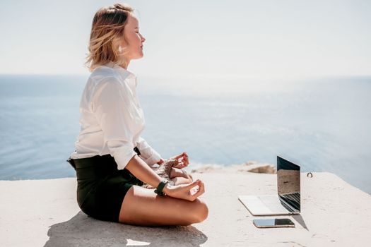 Happy girl doing yoga with laptop working at the beach. beautiful and calm business woman sitting with a laptop in a summer cafe in the lotus position meditating and relaxing. freelance girl remote work beach paradise