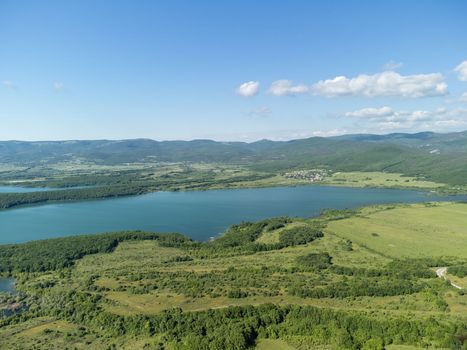 Aerial landscape from flying drone storage reservoir at mountain foot covered colorful spring forest. Beautiful view from above blue lake among highlands
