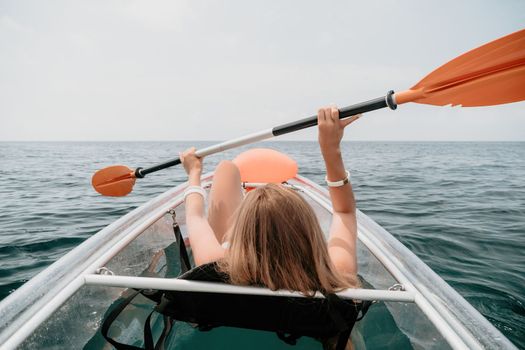 Woman in kayak back view. Happy young woman with long hair floating in transparent kayak on the crystal clear sea. Summer holiday vacation and cheerful female people having fun on the boat.