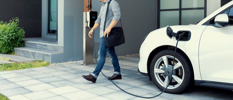 Progressive asian man and electric car with home charging station. Concept of the use of electric vehicles in a progressive lifestyle contributes to a clean and healthy environment.