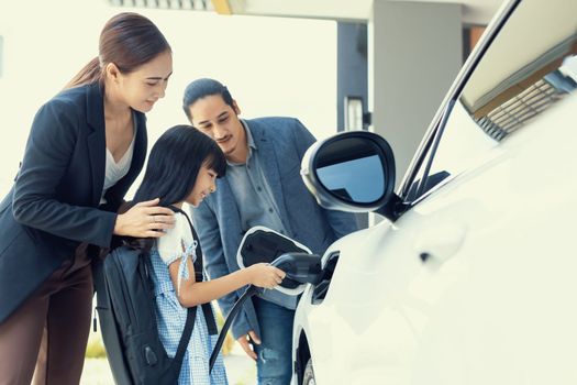 Progressive young parents and daughter with electric vehicle and home charging station. Green and clean energy from electric vehicles for healthy environment. Eco power from renewable source at home.