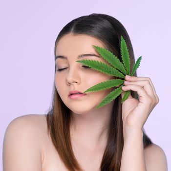 Closeup portrait of charming girl with fresh skin holding green leaf for beauty skin care made from cannabis leaf. Cosmetology and cannabis concept with isolated background.