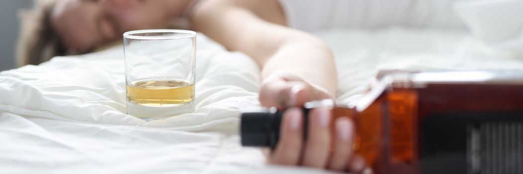Drunk young woman lies in bed in bottle of alcohol. Female alcoholism and depression concept