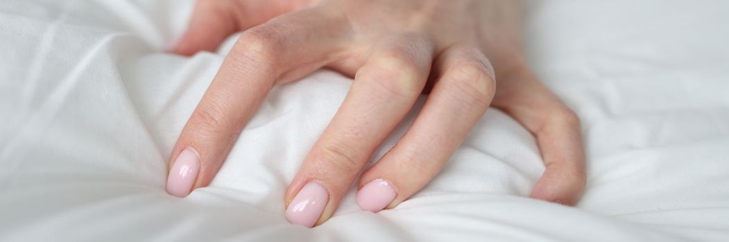 Woman hand tightly grips white sheet on bed. Nightmares and temper tantrums in the morning