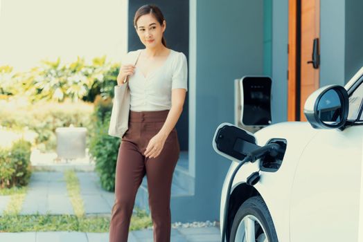Progressive asian woman and electric car with home charging station. Concept of the use of electric vehicles in a progressive lifestyle contributes to a clean and healthy environment.