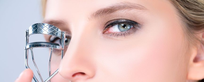 Closeup alluring facial makeup, beautiful woman with perfect smooth cosmetic clean skin correct eyelash curler with metal mechanic beauty accessory in isolated background.