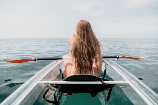 Woman in kayak back view. Happy young woman with long hair floating in transparent kayak on the crystal clear sea. Summer holiday vacation and cheerful female people having fun on the boat.