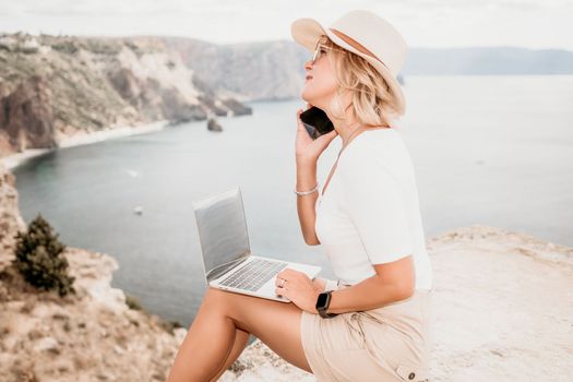 Digital nomad, Business woman working on laptop by the sea. Pretty lady typing on computer by the sea at sunset, makes a business transaction online from a distance. Freelance remote work on vacation