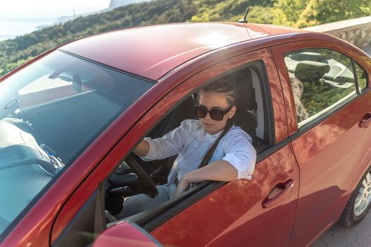 Woman driving a car. A lady in sunglasses takes the wheel of her new car. Rides along the road against the backdrop of mountains and the sea