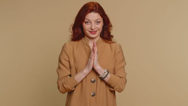 Sneaky cunning redhead woman with tricky face gesticulating and scheming evil plan, thinking over devious villain idea, cheats, revenge, jokes, pranks. Young girl isolated on beige studio background