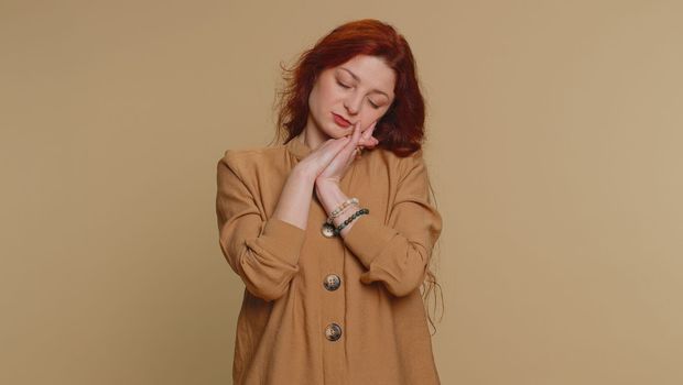 Tired redhead woman yawning, sleepy inattentive feeling somnolent lazy bored overworked gaping suffering from lack of sleep. Young exhausted ginger girl isolated alone on beige studio background