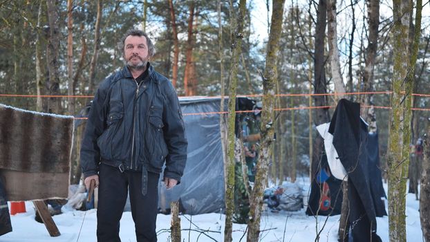A homeless man poses in the woods in front of his hut