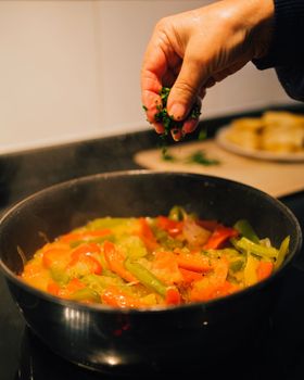 Chef hand adding parsley to a vegetable stir fry. Healhy food cooking concept.