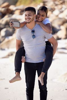 Couple, piggyback and selfie on the beach to have fun and bond with love and affection. Man, woman and ocean date while taking a mobile photo on the sea sand for romance and tropical holiday.
