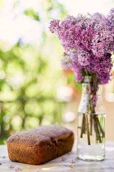 Bouquet of lilacs stands in a bottle on the balcony next to homemade bread. High quality photo