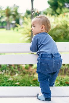 Little girl stands leaning on a white wooden fence in the park. High quality photo