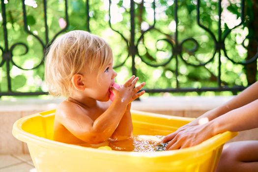 Small child with a toy in his hands sits in a basin of water on the balcony. High quality photo