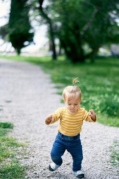 Little girl walks along the gravel path in the park and looks under her feet. High quality photo