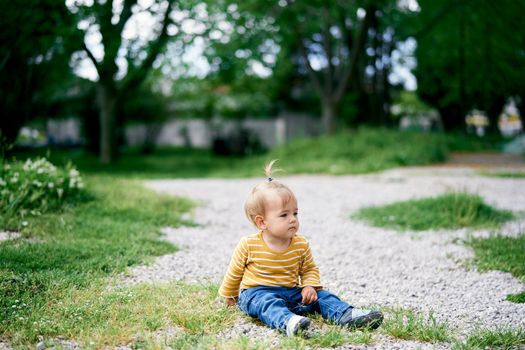 Little serious girl sitting on a gravel path in the park. High quality photo