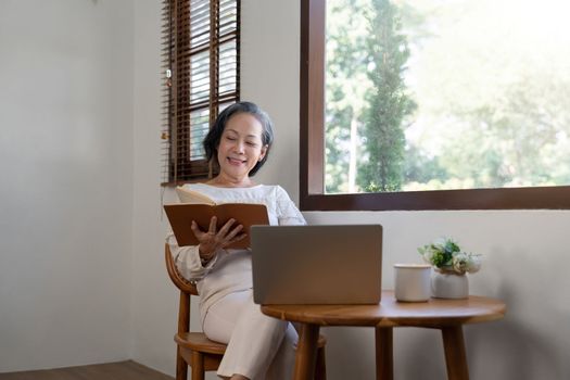 Asian elderly woman relaxing retired reading a book in home living room.