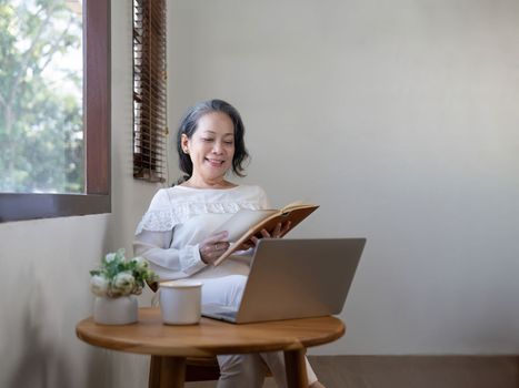 Asian elderly woman relaxing retired reading a book in home living room.